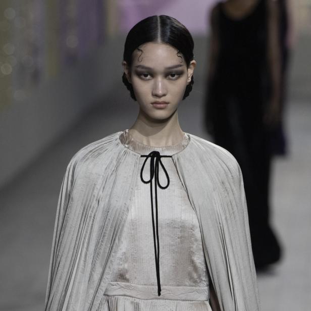 Ein Model präsentiert ein plissiertes Kleid mit Cape auf dem Laufsteg von Christian Dior.