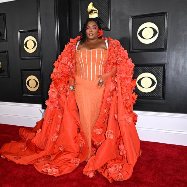 Lizzo in einem orangefarbenen Kleid mit Blumenapplikationen auf dem roten Teppich der Grammy Awards.