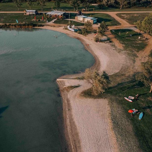 Luftaufnahme eines Sees mit Sandstrand und einem kleinen Boot auf dem Wasser.