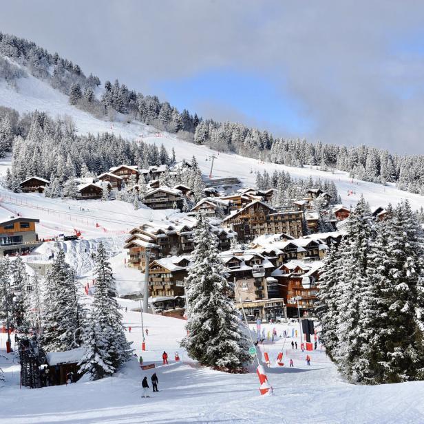 Blick auf ein verschneites Skidorf mit Skipisten und bewaldeten Hängen.