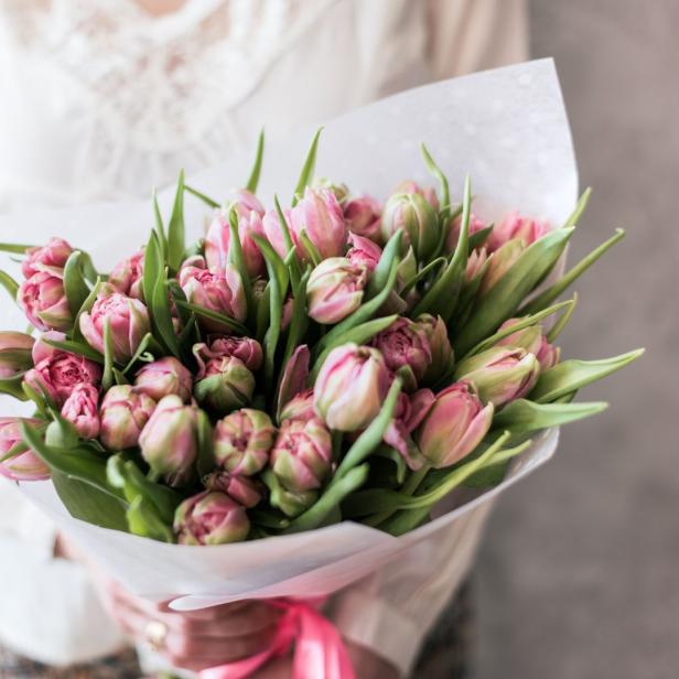 Eine Person hält einen Strauß rosa Tulpen in der Hand.