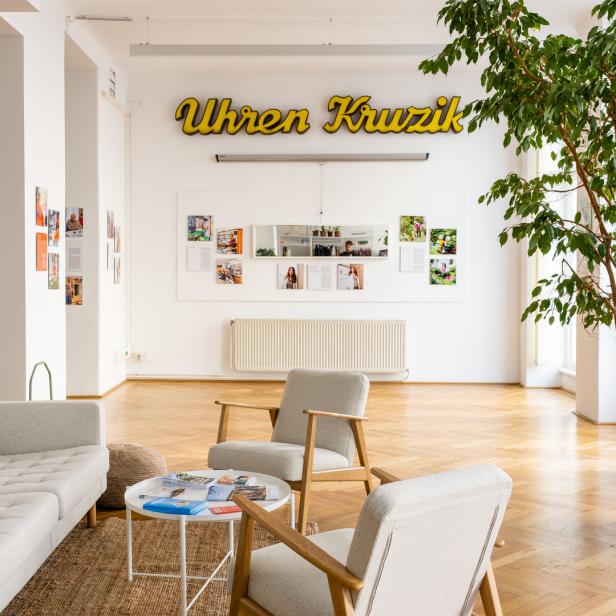 Ein heller Raum mit Sitzgelegenheiten und dem Schriftzug „Uhren Kruzik“ an der Wand.