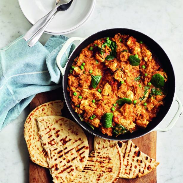 Ein Gericht mit Hühnchen-Curry, Naan-Brot und Reis auf einem Tisch.
