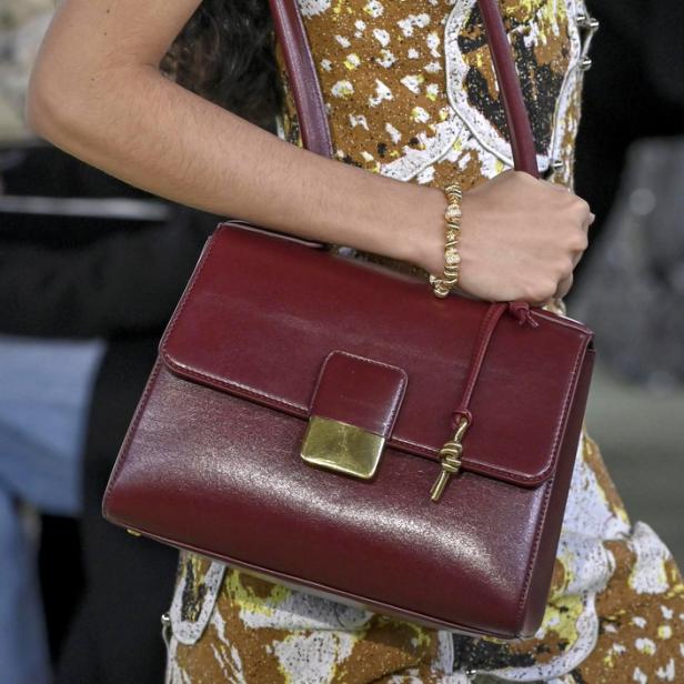 Eine Frau trägt eine bordeauxrote Handtasche mit goldenen Akzenten.