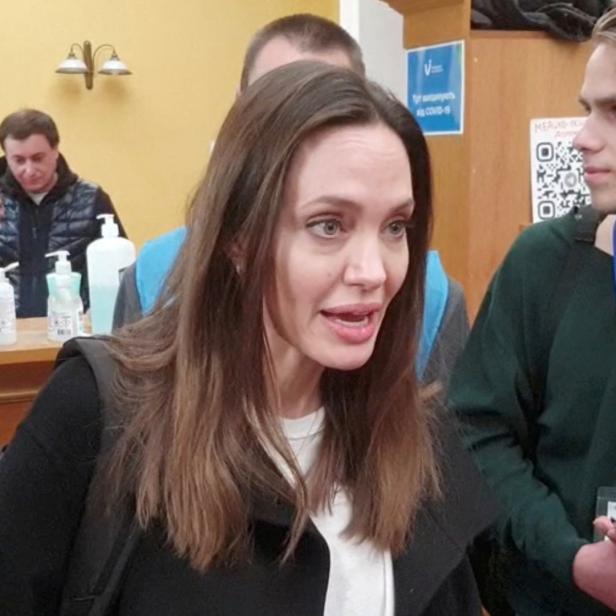 Angelina Jolie spricht mit einem jungen Mann in einem Innenraum.