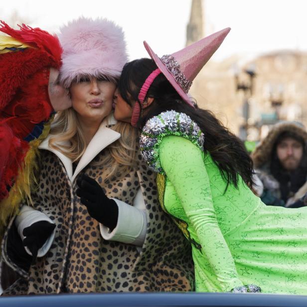 Eine Frau in Leopardenmuster wird von einem Papagei und einer Hexe auf einer Parade geküsst.