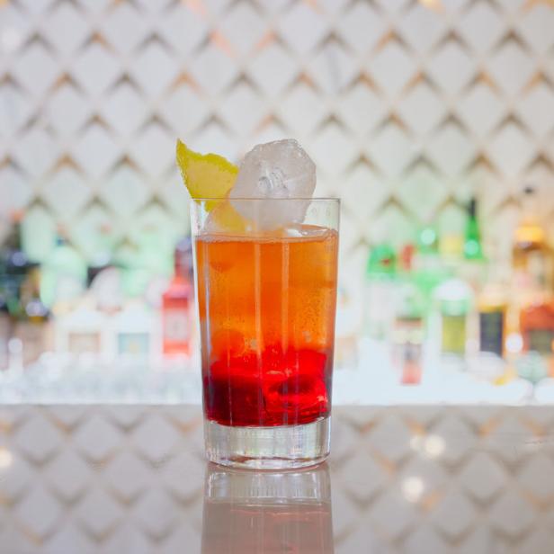 Ein Cocktail mit Eiswürfel und Zitronenzeste steht auf einer Bar.