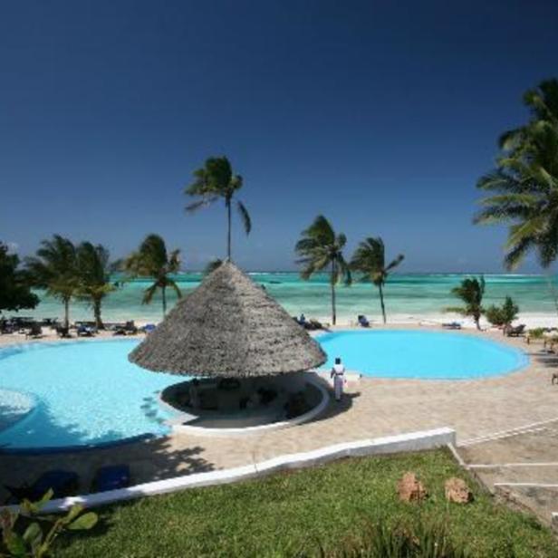 Ein Resort mit einem Pool, einer Bar mit Strohdach und Palmen am Strand.