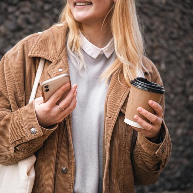 Nahaufnahme, eine Tasse Kaffee und ein Smartphone in weiblichen Händen in der Stadt.