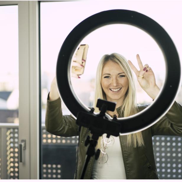 Eine Frau macht ein Selfie mit einem Ringlicht und zeigt das Victory-Zeichen.