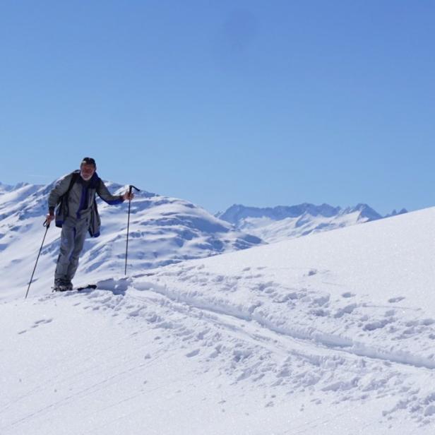Ein Mann wandert mit Skiern und Stöcken durch eine verschneite Berglandschaft.
