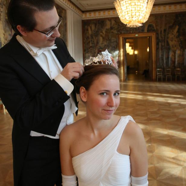 Ein Mann im Smoking setzt einer Frau im weißen Kleid eine Tiara auf.