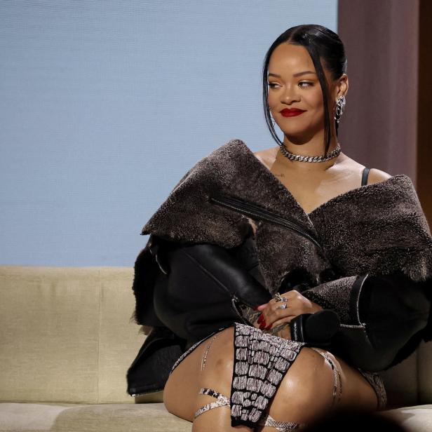 Rihanna sitzt auf einem Sofa und lächelt.