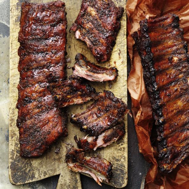 Spareribs, teilweise geschnitten, liegen auf einem Holzbrett und braunem Papier.