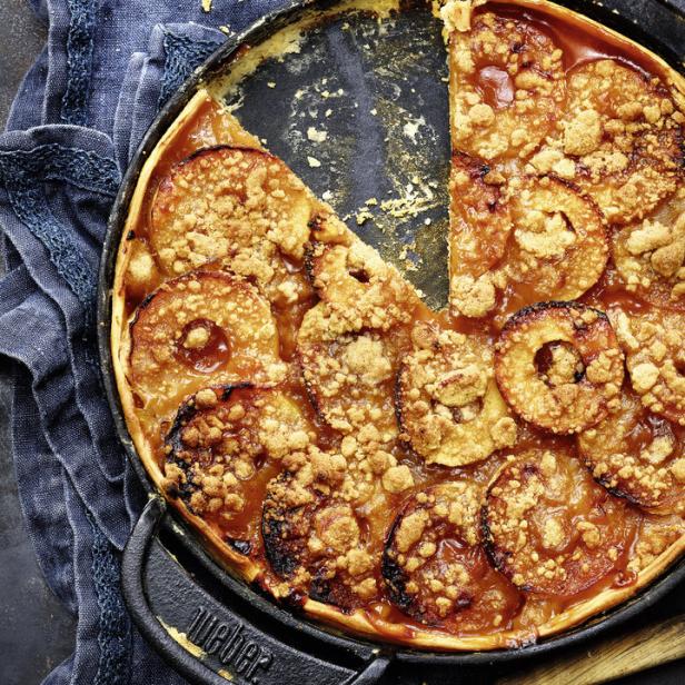 Ein Apfelkuchen mit Streuseln in einer schwarzen Pfanne, ein Stück fehlt.