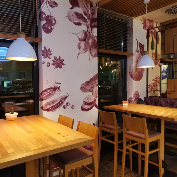 Innenansicht eines Restaurants mit Holztischen und floralen Wandmalereien.