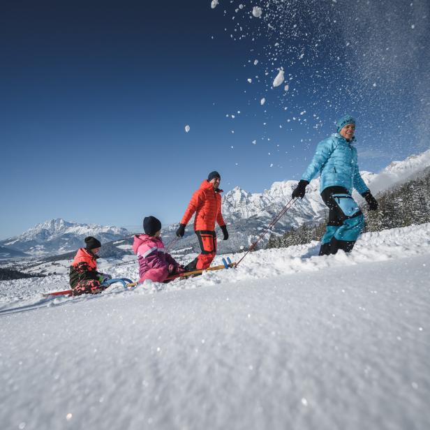 Eine Familie zieht einen Schlitten im Schnee vor einer Bergkulisse.