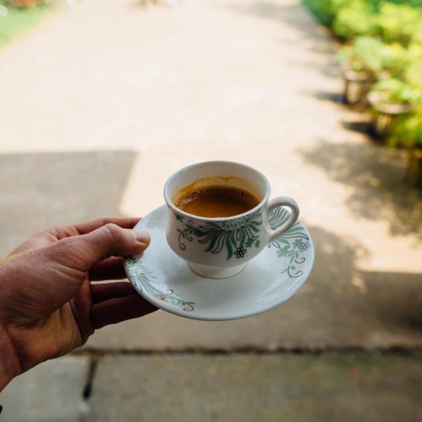 Eine Hand hält eine Tasse Kaffee auf einer verzierten Untertasse.