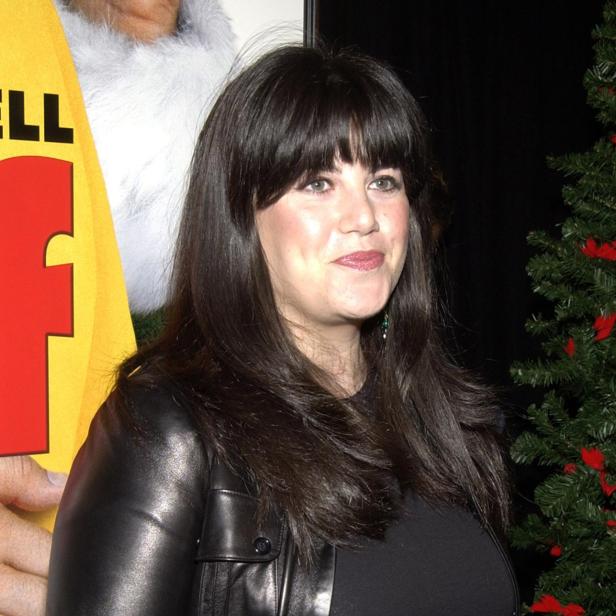 Eine Frau in Lederjacke posiert neben einem Weihnachtsbaum und einer Filmplakatwand.
