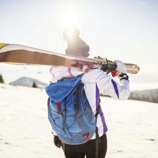 Eine Skifahrerin mit Rucksack trägt ihre Skier über der Schulter.