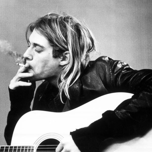Kurt Cobain mit Gitarre und Zigarette in Schwarzweiß.