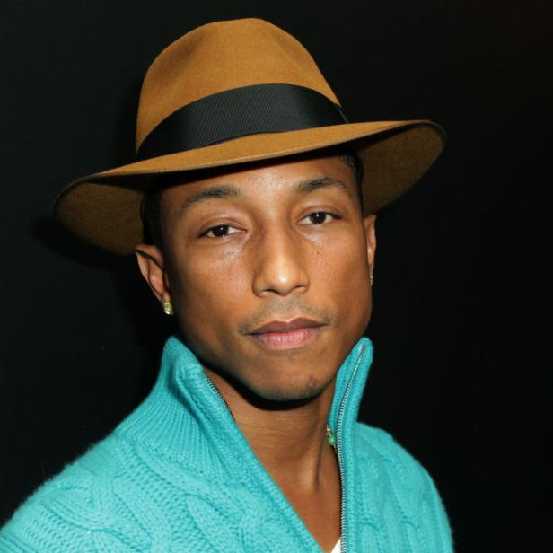 Pharrell Williams mit Hut und türkisfarbenem Pullover vor schwarzem Hintergrund.