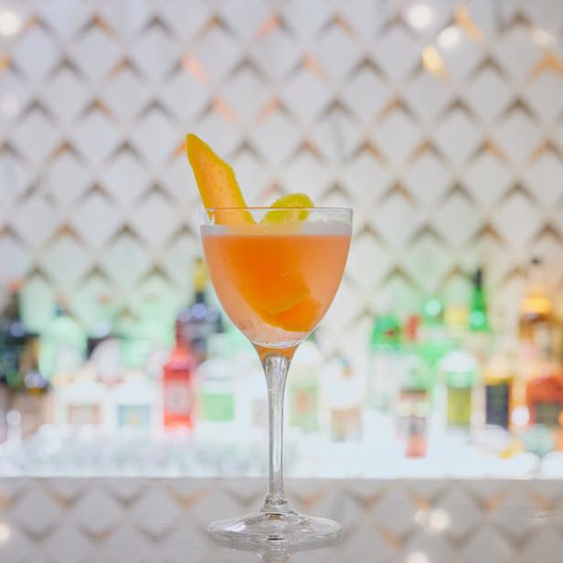 Ein Cocktail in einem Glas mit Melonenschale als Dekoration steht auf einer Bar.