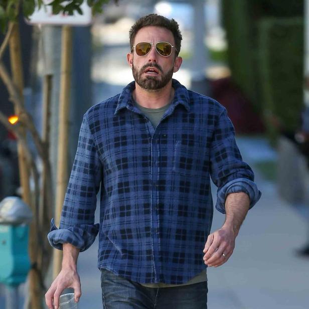 Ben Affleck geht mit einem Getränk in einem Glas auf der Straße entlang.