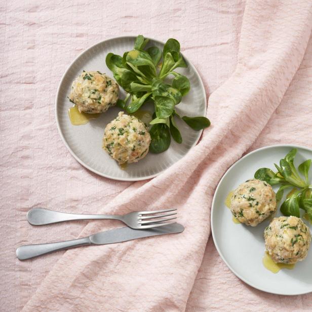 Zwei Teller mit Serviettenknödeln und Feldsalat auf einem rosa Tuch.
