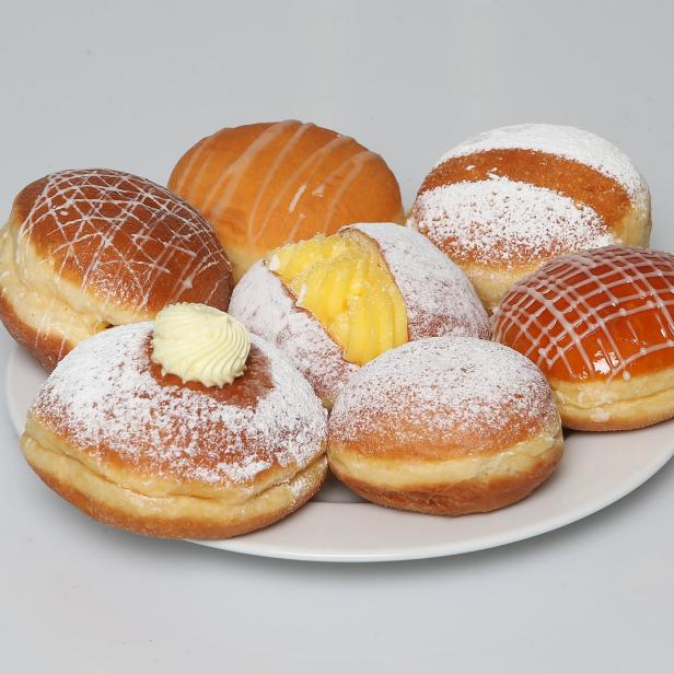 Auf einem Teller liegen verschiedene Berliner, einige mit Puderzucker, andere mit Guss oder Marmelade.