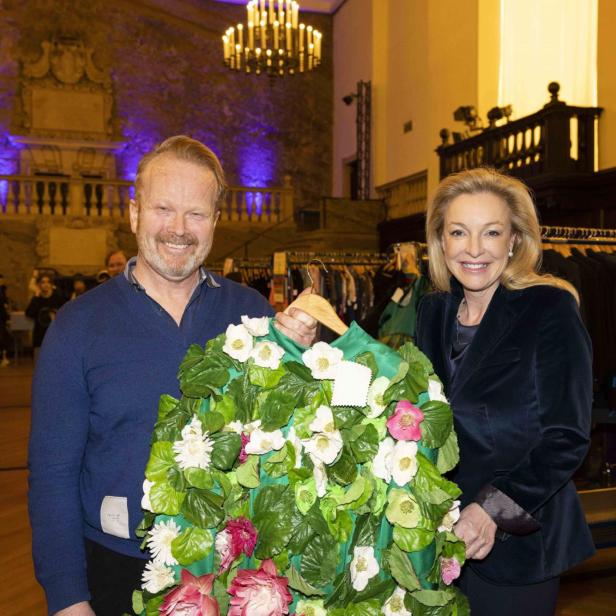 Zwei Personen halten eine Jacke, die mit Blumen und Blättern verziert ist.