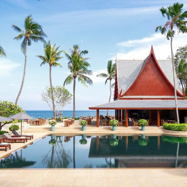 Ein Pool spiegelt ein Gebäude im thailändischen Stil und Palmen wider.