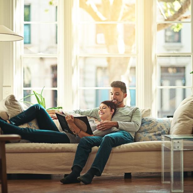 Ein Paar entspannt auf einem Sofa und liest gemeinsam ein Buch.