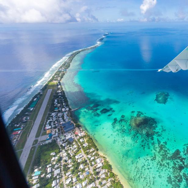 Luftaufnahme eines tropischen Atolls mit türkisfarbenem Wasser und einem Flugzeugflügel im Vordergrund.