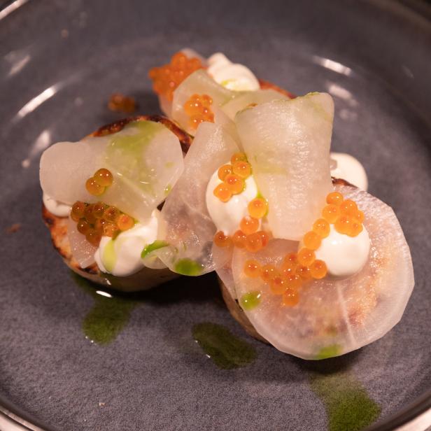 Drei Canapés mit Rettich, Creme und orangefarbenem Fischrogen auf einem Teller.