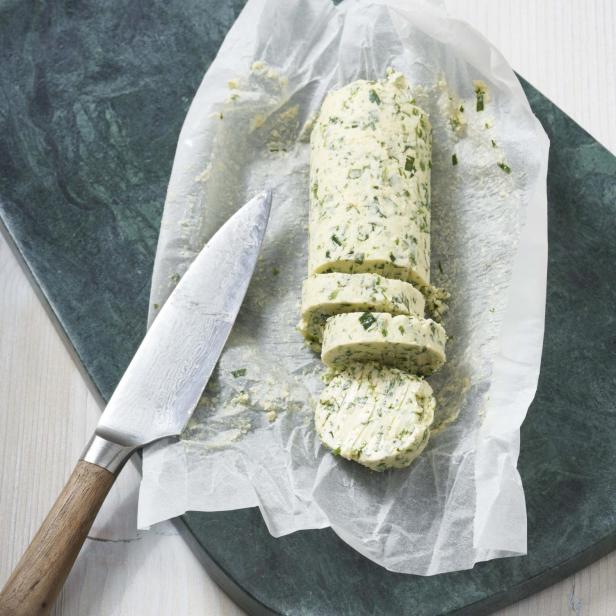 Kräuterbutter wird in Scheiben geschnitten auf einem Schneidebrett präsentiert.