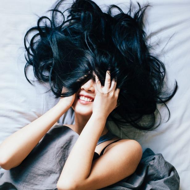 Eine Frau mit langen, dunklen Haaren liegt lächelnd im Bett.