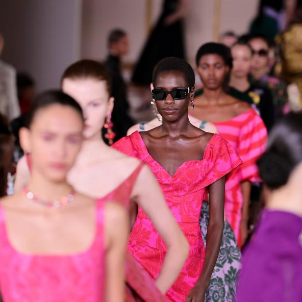 Eine Modenschau mit Models in farbenfrohen Kleidern, darunter ein pinkfarbenes Kleid mit Blumenmuster.