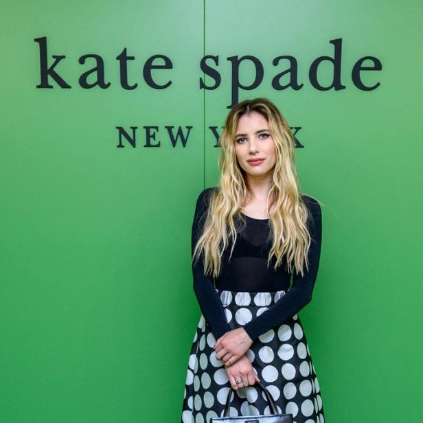 Emma Roberts posiert vor einem grünen „Kate Spade New York“-Hintergrund.