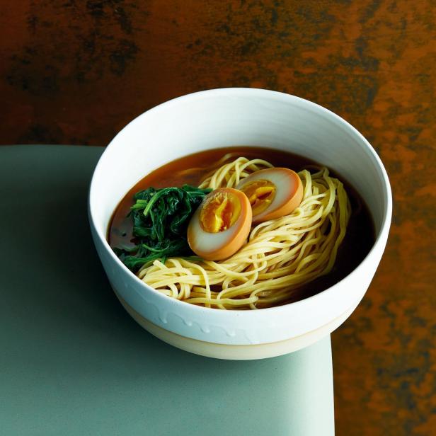 Eine Schüssel Ramen mit Nudeln, Ei und Gemüse steht auf einem Tisch.