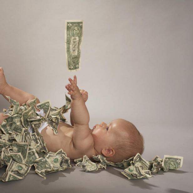 Ein Baby liegt auf dem Rücken, bedeckt mit US-Dollar-Scheinen, die von oben fallen.