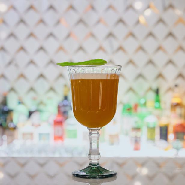 Ein bernsteinfarbener Cocktail in einem eleganten Glas, garniert mit einem Blatt.