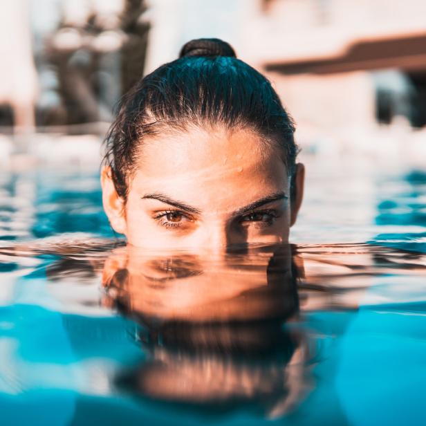 Eine Frau ist bis zum Hals in blauem Wasser und blickt in die Kamera.