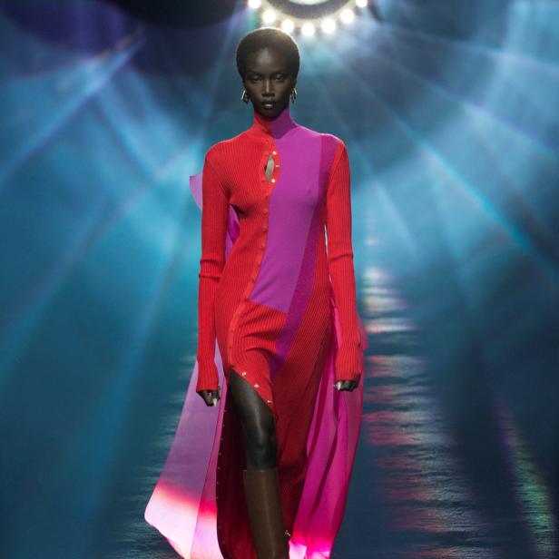 Eine Frau in einem rot-pinken Kleid und braunen Stiefeln auf einem Laufsteg.