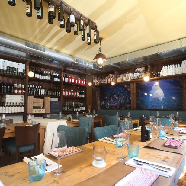 Innenansicht eines Restaurants mit gedeckten Holztischen und Weinregalen.