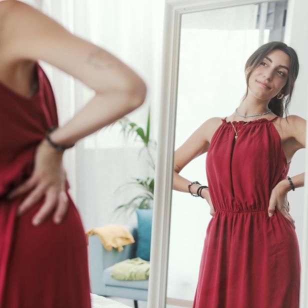 Eine Frau probiert ein rotes Kleid vor dem Spiegel an.