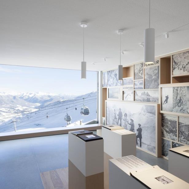 Ein Ausstellungsraum mit Blick auf eine verschneite Berglandschaft mit Seilbahnen.