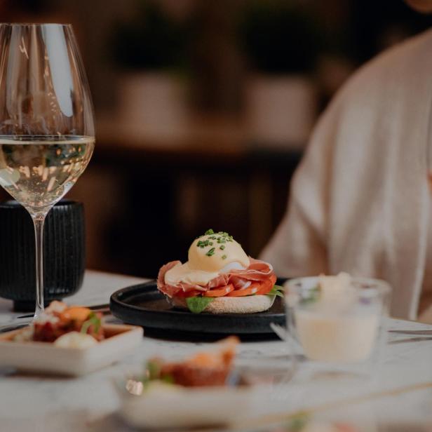 Ein gedeckter Tisch mit Speisen, darunter ein Glas Weißwein und Eggs Benedict.