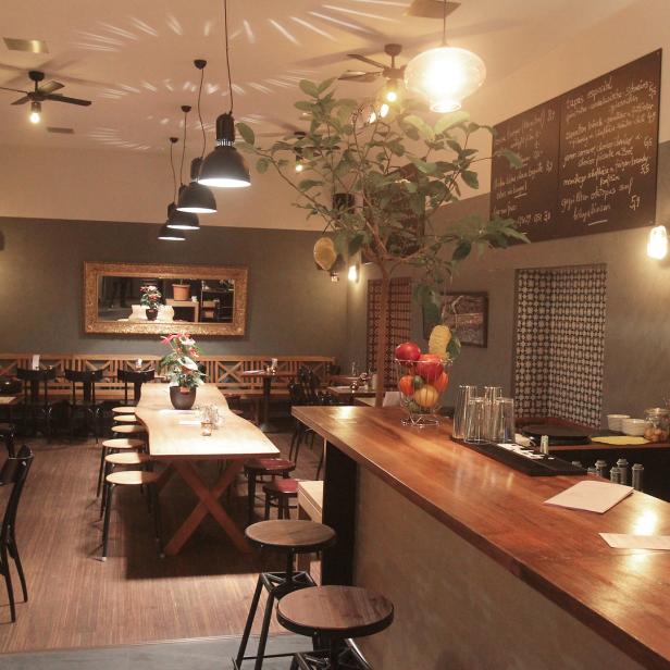 Innenansicht eines Restaurants mit Holztischen, Stühlen und einer Bar.
