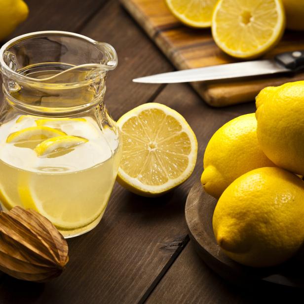 Ein Krug Zitronenlimonade mit Zitronen und einer Zitruspresse auf einem Holztisch.